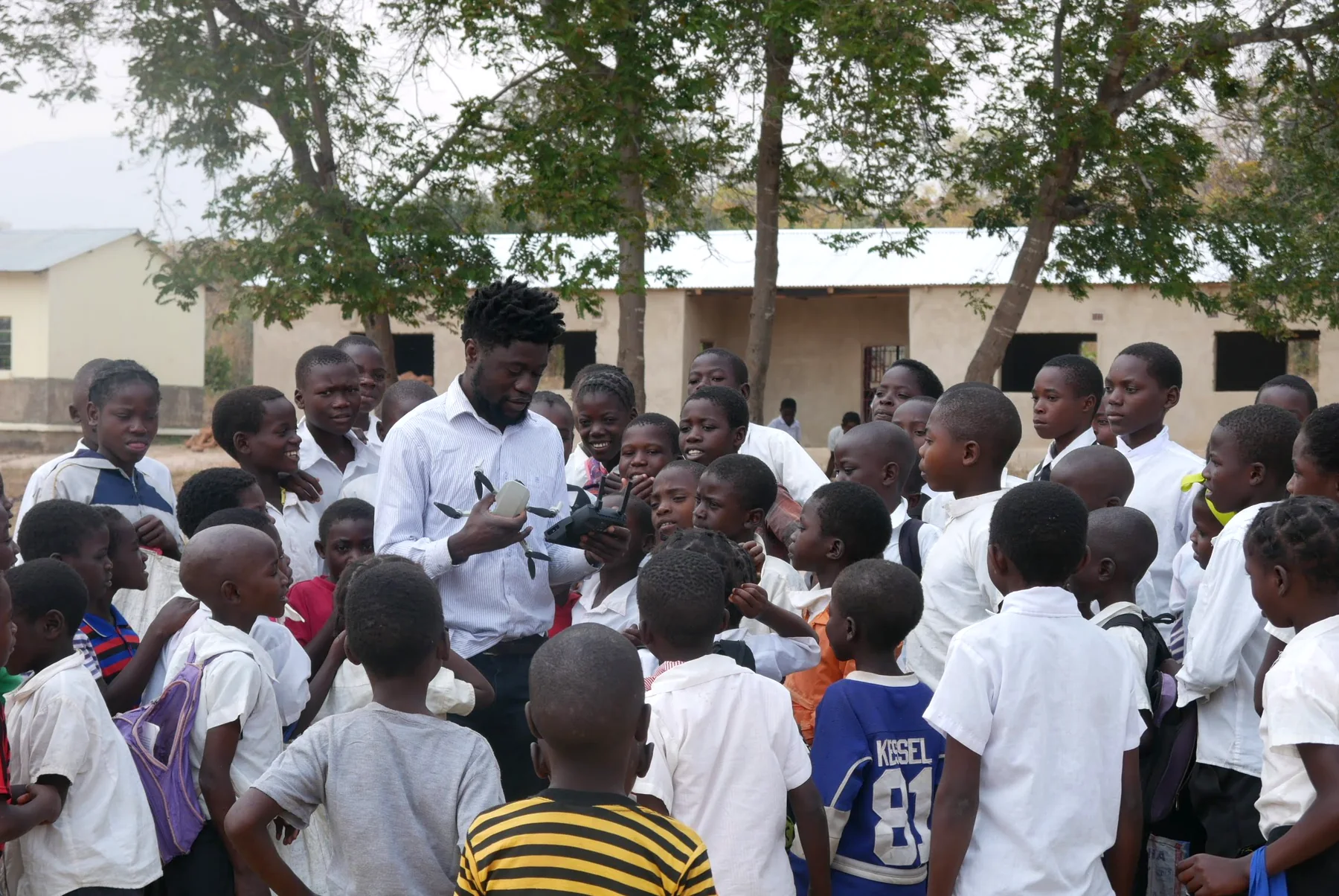 Victor demonstrating a DJI Mavic Mini drone and controller to a group of pupils at Mwiniwise Combined School
