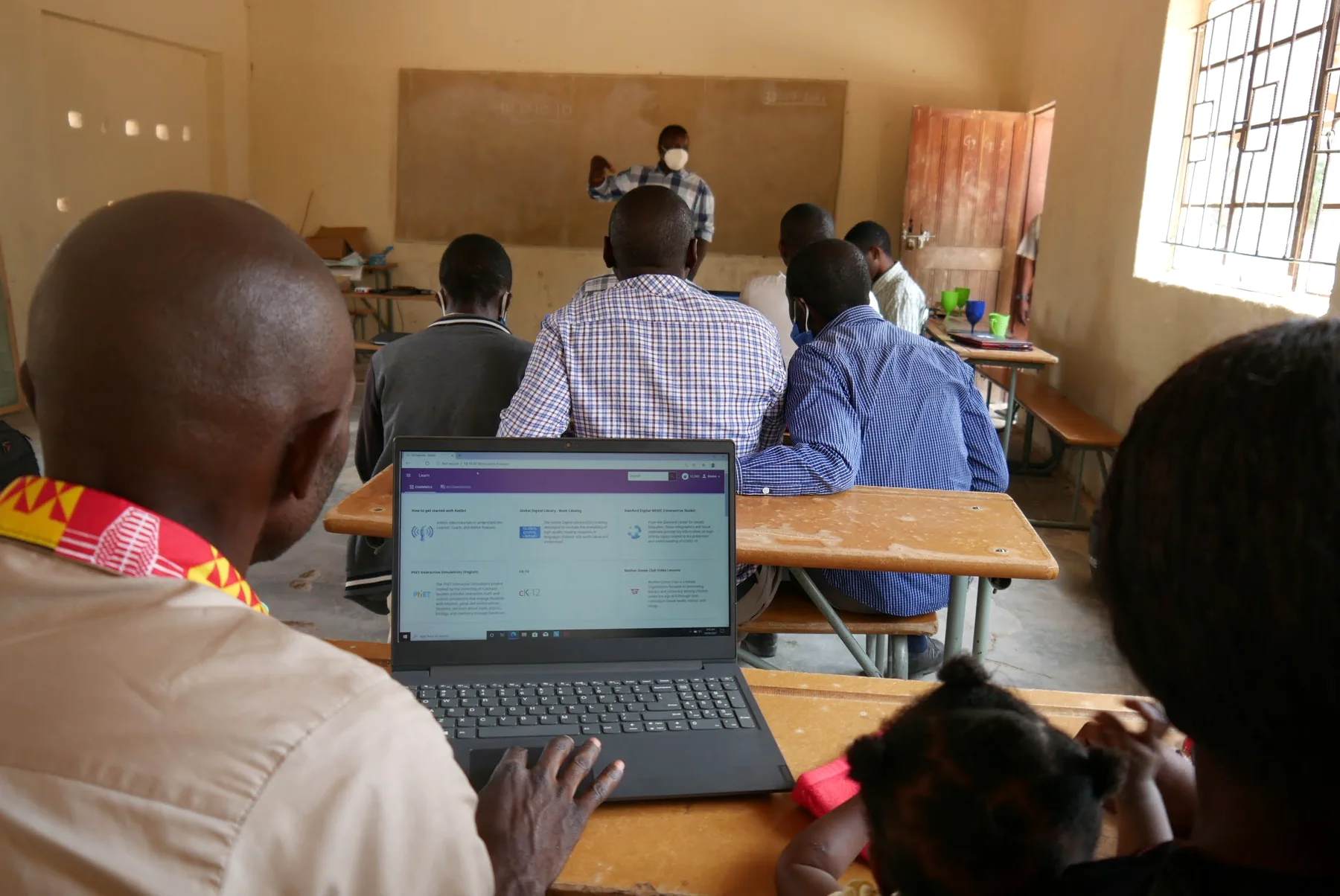 Enock presenting at the front of a classroom as teachers participate in a digital learning workshop