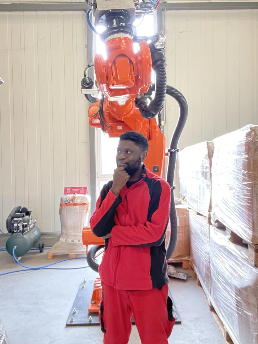 Victor standing in a workshop in front of a large orange ABB industrial robot with cable-routing equipment